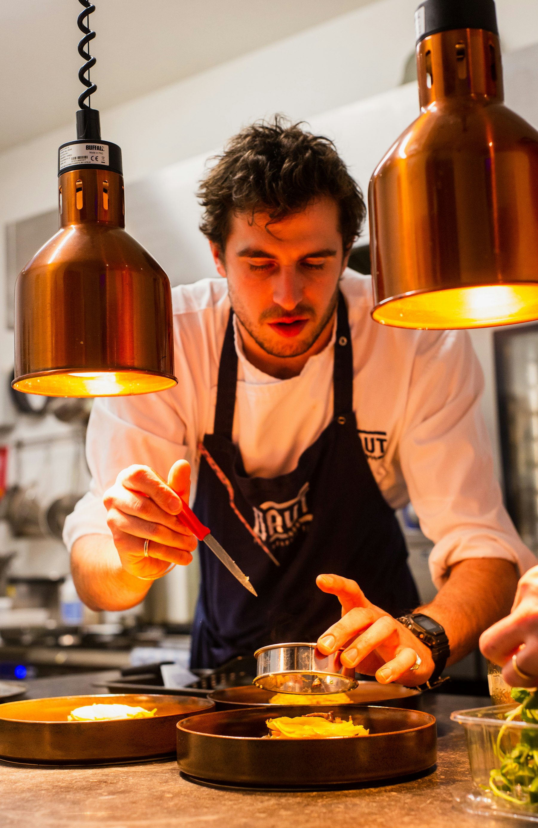 A chef finishing a plate under warm copper lamps